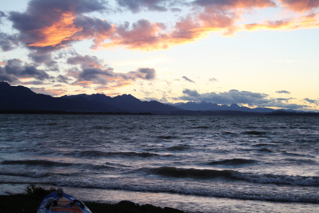 Der Chiemsee in Bayern bei einem tiefroten Sonnenuntergang nach einem Sturm. Es sind noch viele wellen am Chiemsee zu sehen.