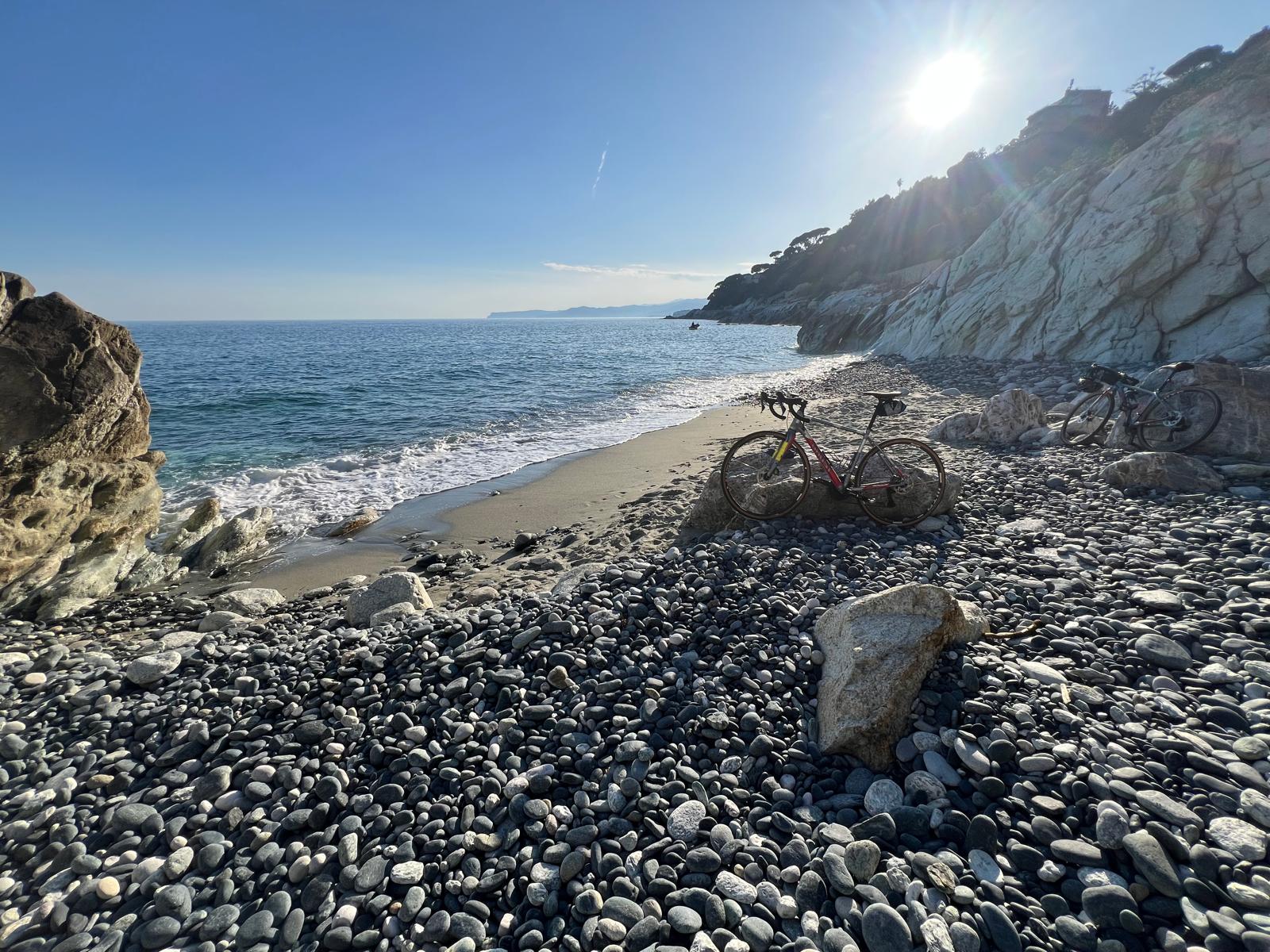 Ein Gravelbike steht am Schotterstrand in einer einsamen Bucht in Ligurien am Meer.