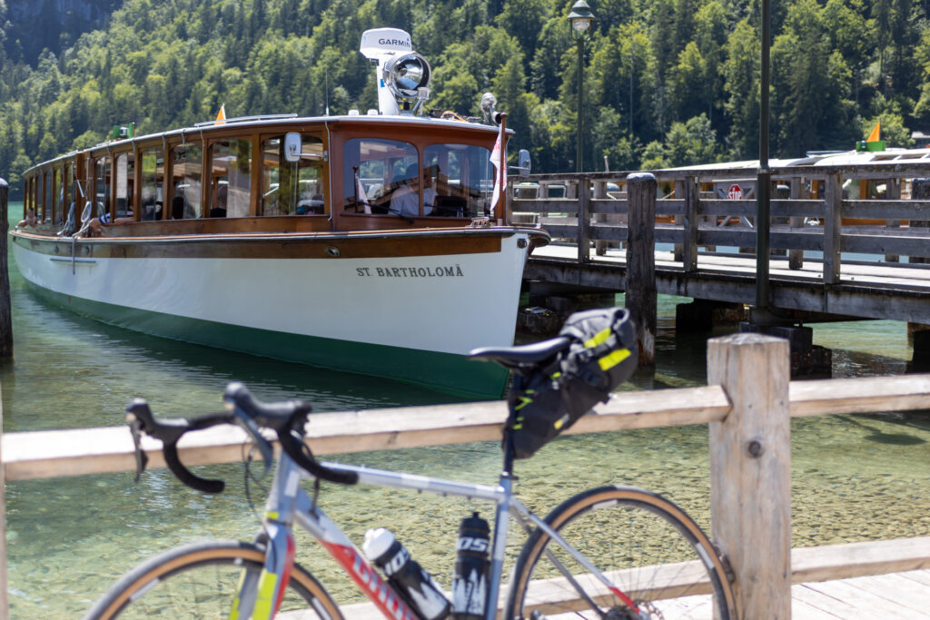 Ein Schiff an der Anlegestelle am Königsee mit einem Gravelbike davor.