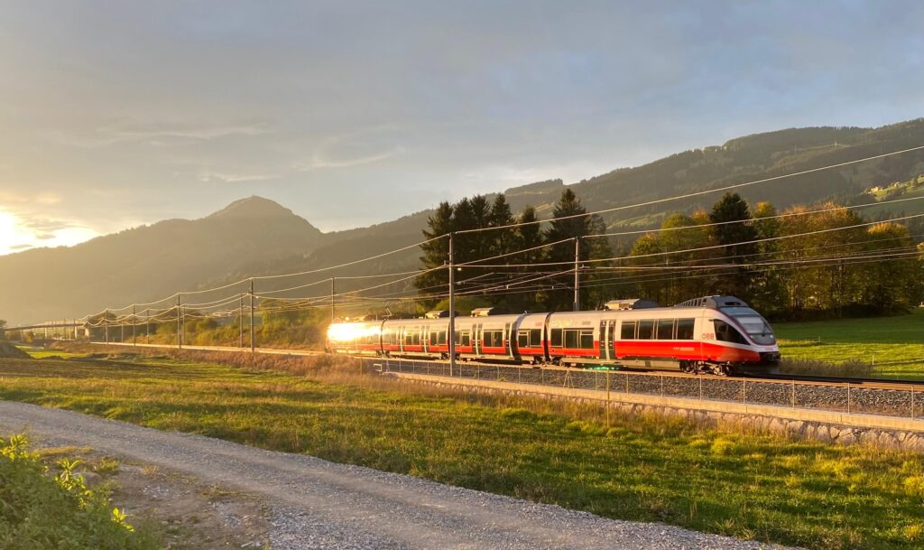 Mit dem Klimaticket bis ins Ausland Reisen. Foto mit Zug in einem Alpental bei Sonnenuntergang.