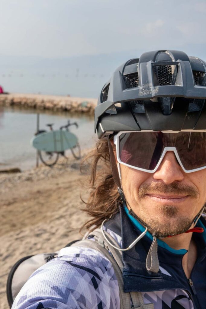 Alpenüberquerung zum Gardasee als Zwischenstopp. Radfahrer im Vordergrund und Gravelbike mit Surfboard im Hintergrund