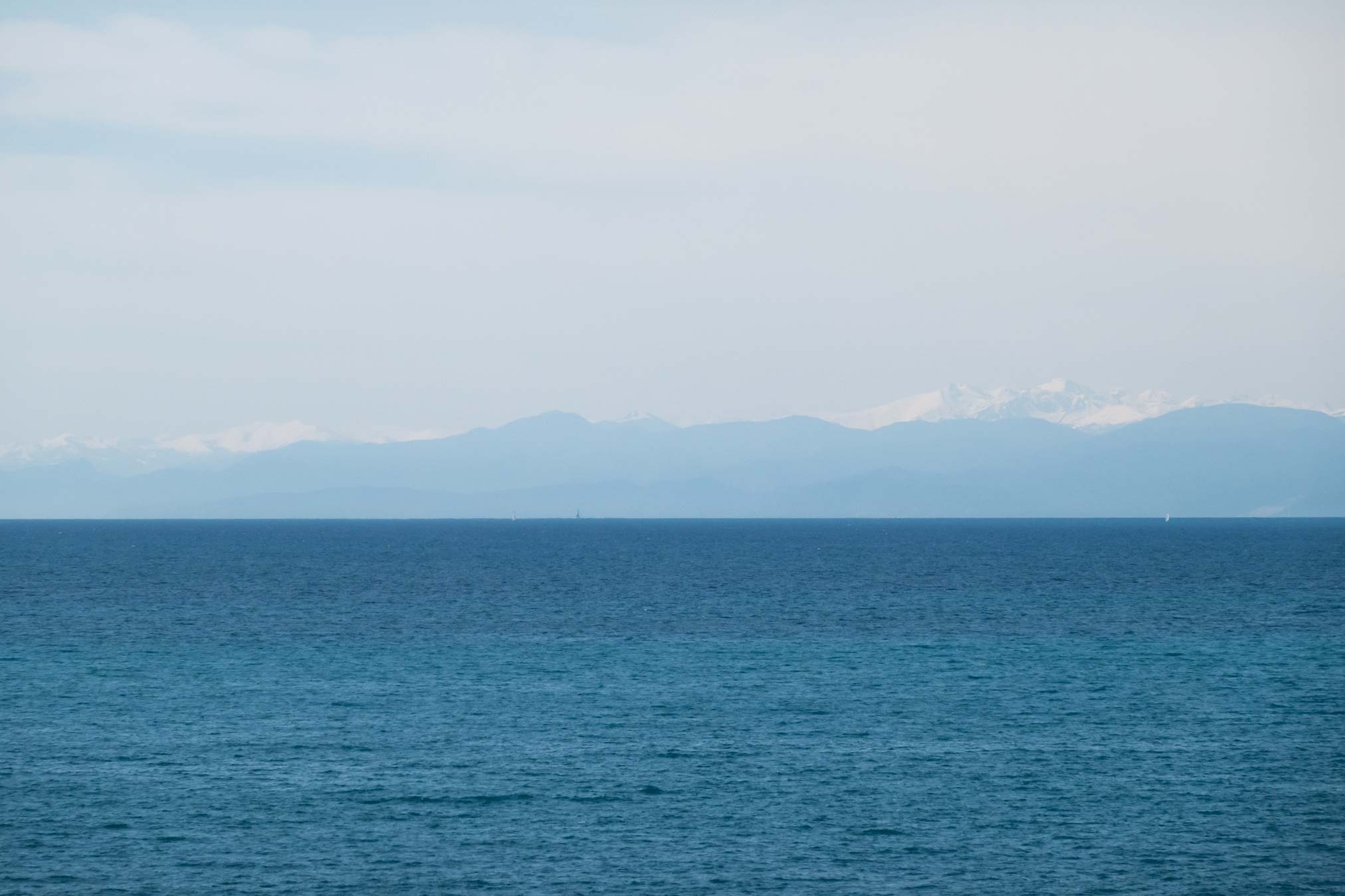 Die ligurische Küste von der Riviera aus fotografiert mit dem Meer und den Alpen hinter Genua.